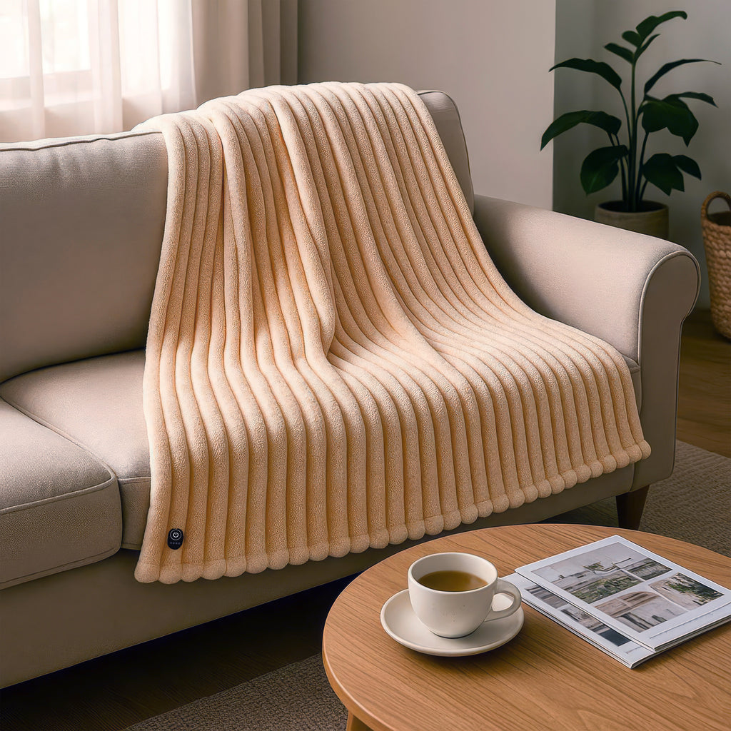 Vanilla Cream blanket (EHHT02VC) draped over a sofa in a cozy living room with a cup of tea and newspaper on a table.